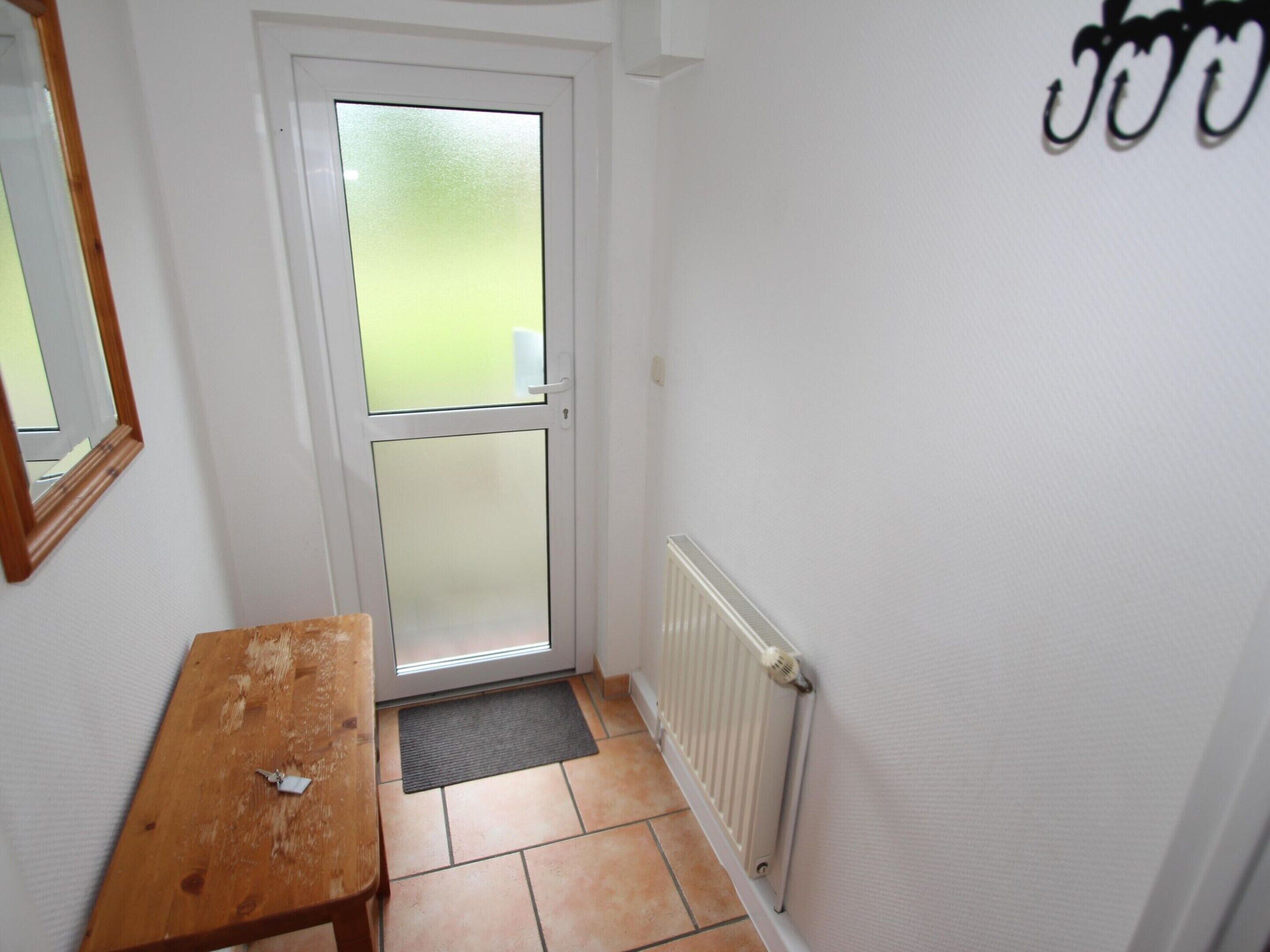 A narrow hallway with a white door, a wooden bench, and a radiator on the wall.