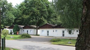Rivi valkoisia mökkejä, joissa on ruskeat katot, ja niiden ympärillä on puita sekä asfaltoitu tie.