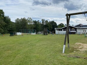 A playground with swings and slides, a small building, and a grassy field. - Ferienhaus in Fassberg mit Einer Terrasse (Faßberg)