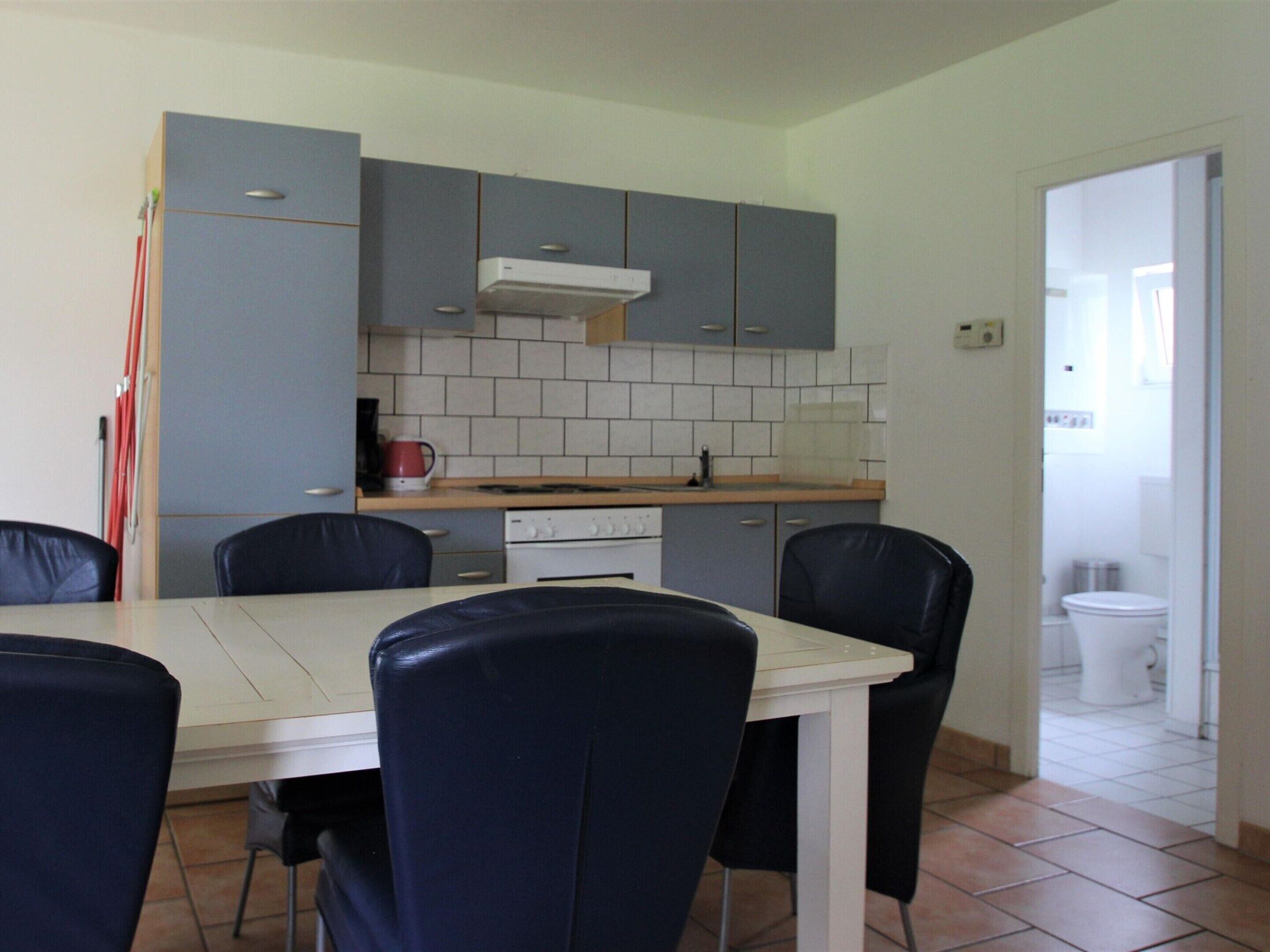 Une cuisine de taille modeste, avec des meubles gris, une cuisinière blanche et une table à manger entourée de quatre chaises.