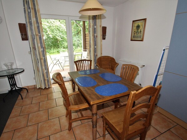A dining area with a wooden table and chairs, a small round table with a glass, and a view through a glass door to an outdoor patio. - Ferienhaus in Fassberg mit Einer Terrasse (Faßberg)