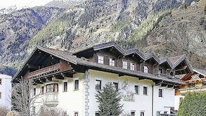 A traditional chalet-style building with multiple windows and a sloped roof, surrounded by mountains and parked cars. - Apartment and Terrace in Langenfeld (Laengenfeld)