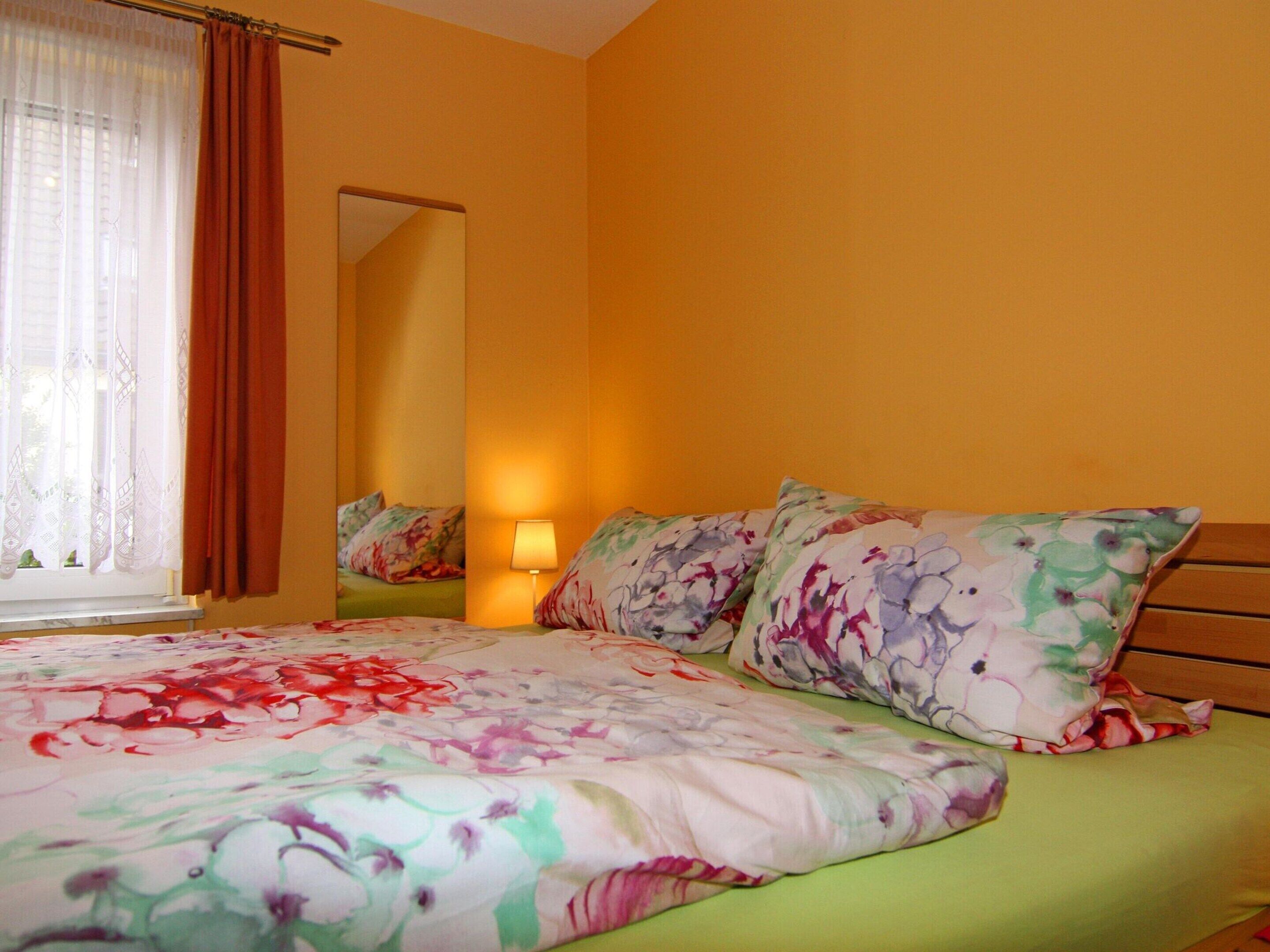 A bedroom with a floral bedspread, a bedside lamp, and a window with curtains.