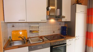 A compact kitchen with white cabinets, a stainless steel sink, a dishwasher, and an oven. - Ferienwohnung im Appartementhaus Stapel, Busum (Büsum)