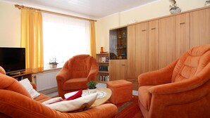 A living room with two orange armchairs, a coffee table, and a bookshelf. - Ferienwohnung im Appartementhaus Stapel, Busum (Büsum)