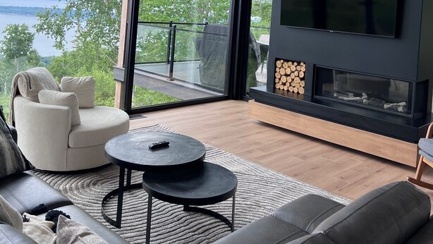 A modern living room with a large TV, a fireplace, and a view of the outdoors. - Le Lord, River view, trail and snowmobile (Les Éboulements)