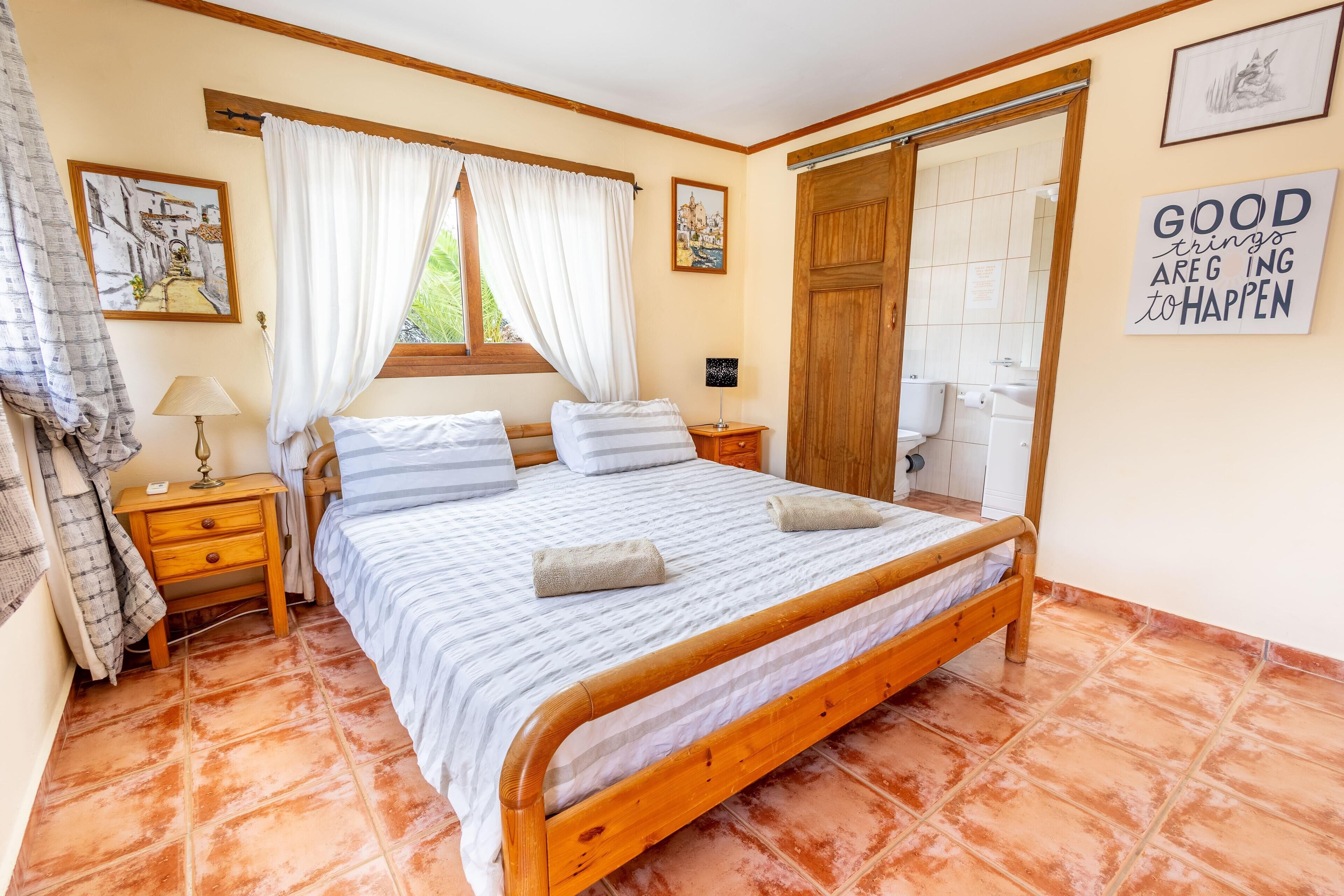 A bedroom with a wooden bed, a nightstand, a lamp, and a window with curtains.