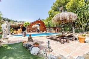 A pool area with lounge chairs, a thatched umbrella, and a wooden cabin. - Luxurious Private Cabin Pool Hottub & Fireplace (Alhaurin el Grande)