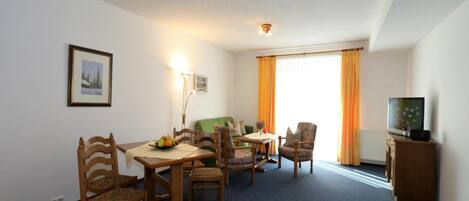 Habitación de hotel con una mesa de comedor, sillas, un sofá, un televisor y una ventana con cortinas.