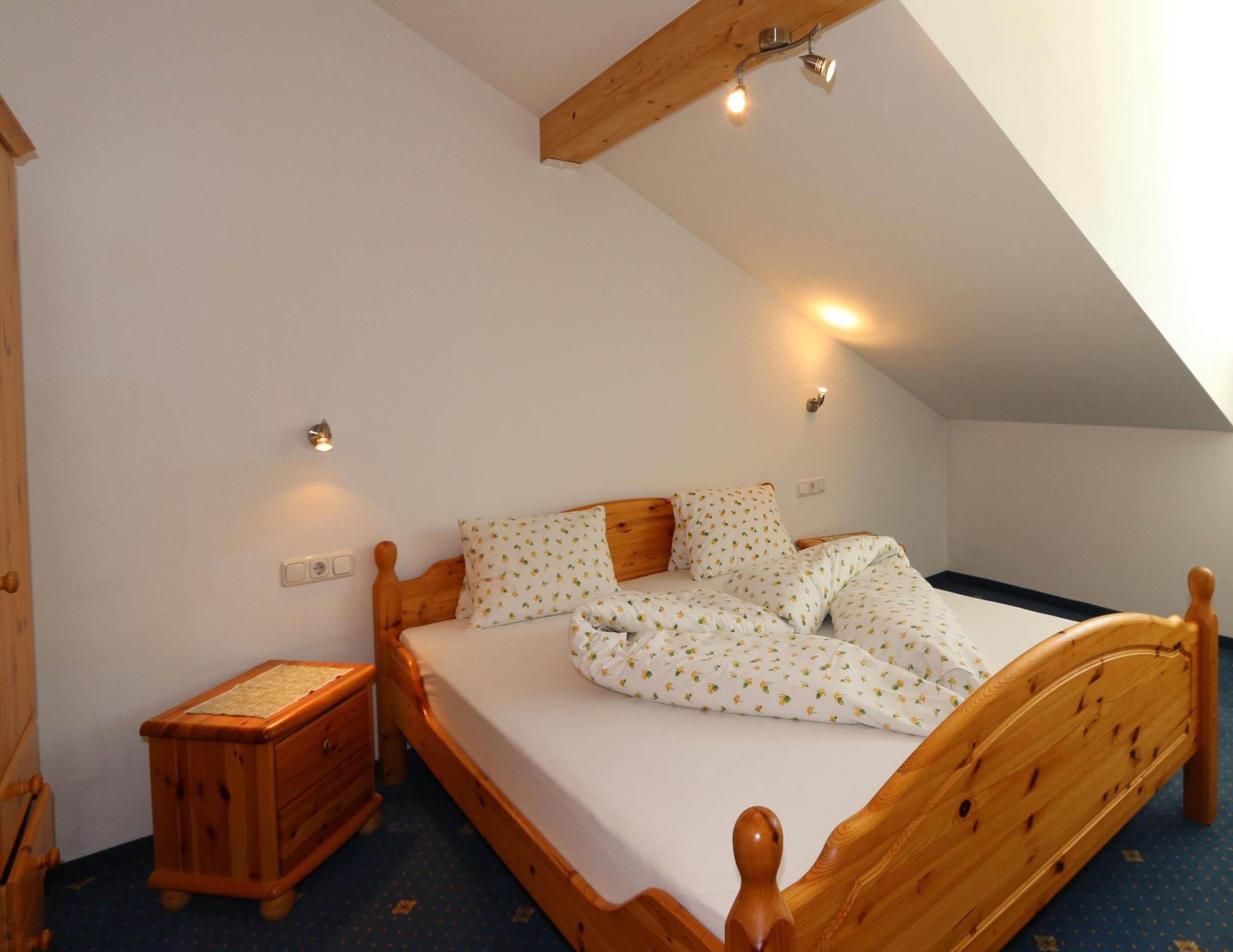 A bedroom with a wooden bed, white bedding, and a sloped ceiling.