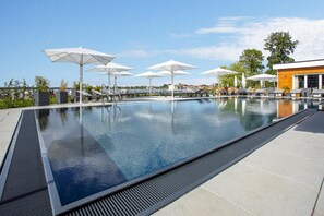 Un espace piscine extérieur moderne, doté de nombreuses chaises longues et de parasols, et entouré d’un ciel dégagé.