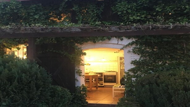 A cozy, well-lit kitchen with a dining area, surrounded by lush greenery and a wooden pergola. - Holiday Home in the Countryside, With Pool, Garden (gmina Bobolice)
