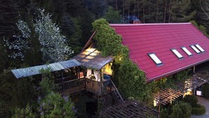 A house with a red roof, a wooden deck, and a covered outdoor area with a metal roof. - Holiday Home in the Countryside, With Pool, Garden (gmina Bobolice)