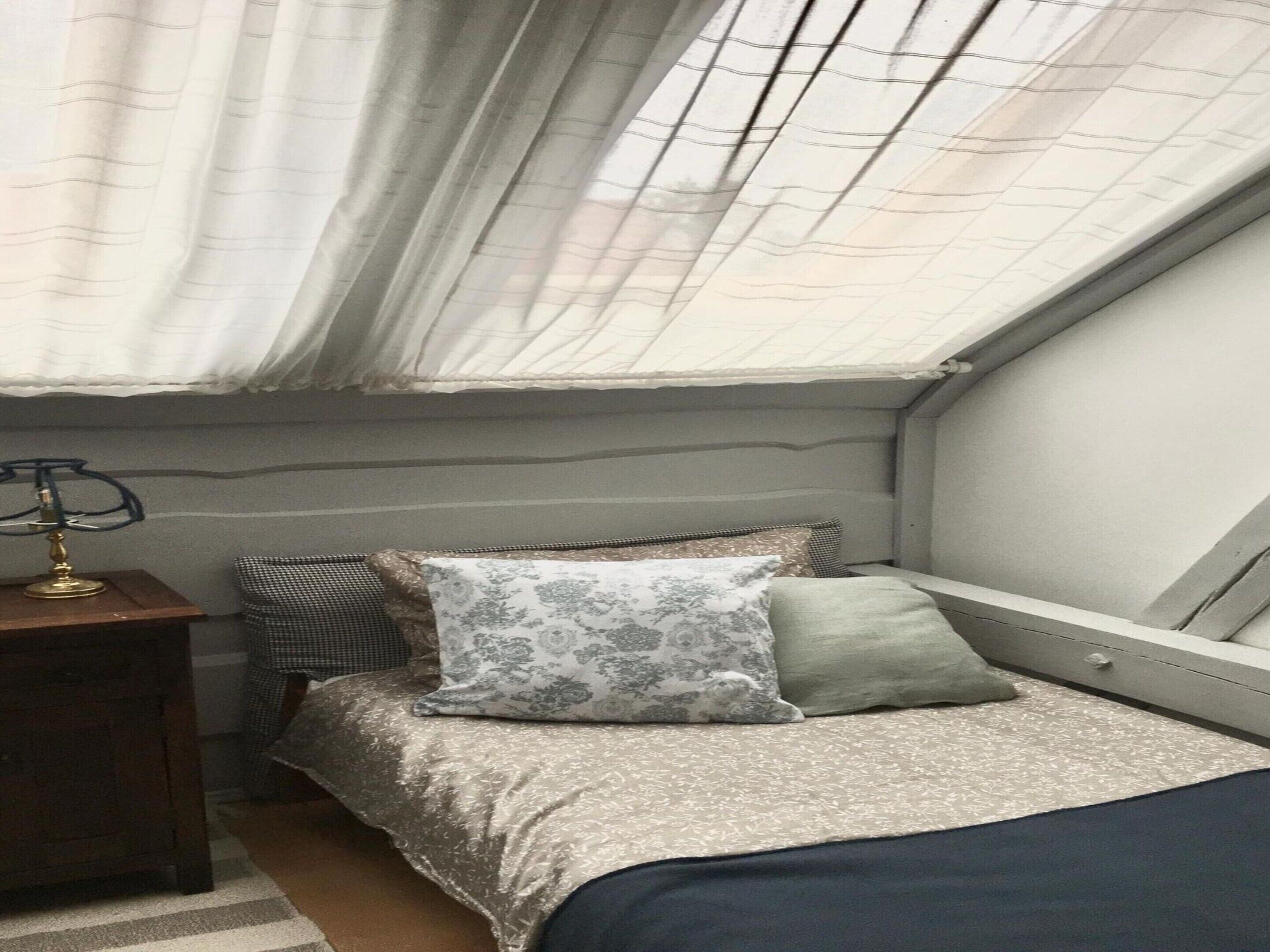 Una camera da letto con un letto, un comodino, una lampada e una finestra con tende.