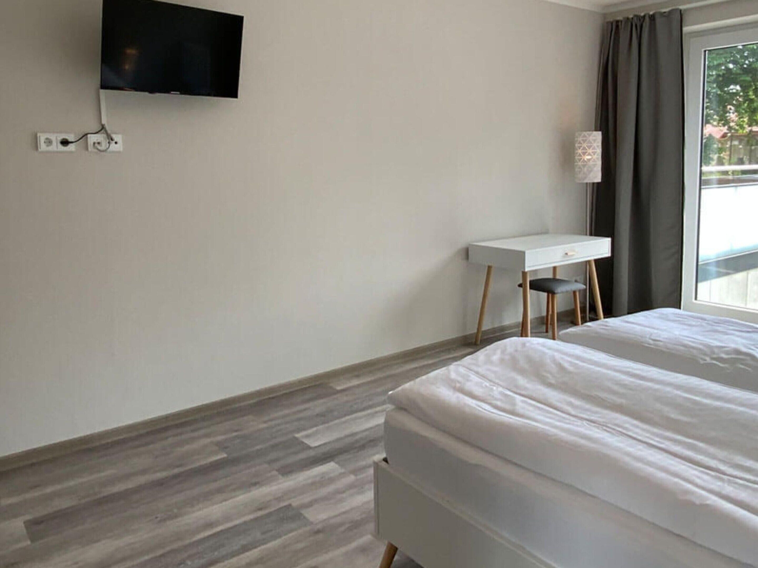 Une chambre d’hôtel comprenant un lit, un bureau, une chaise, un téléviseur fixé au mur et une fenêtre avec des rideaux.