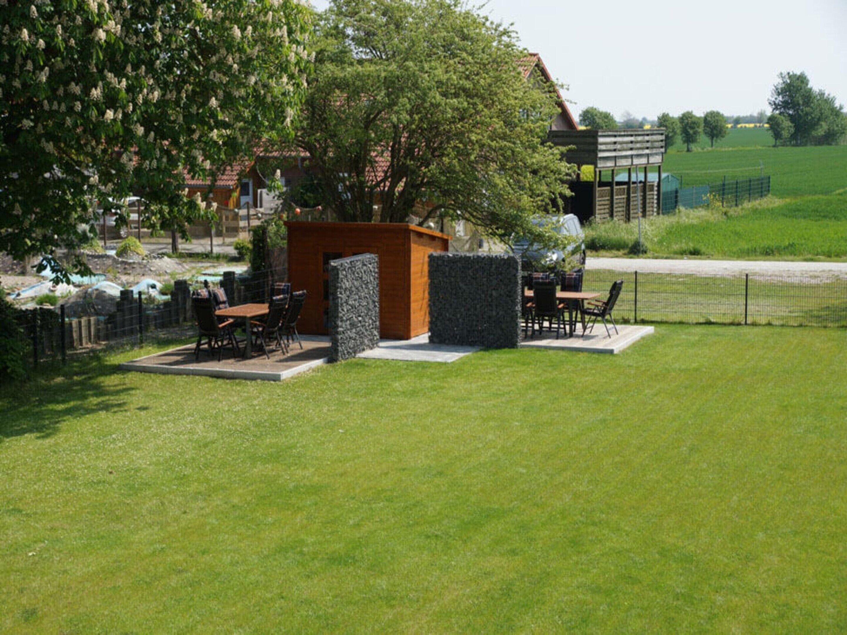 A well-maintained outdoor patio area with a wooden table and chairs, surrounded by a stone wall and a hedge.