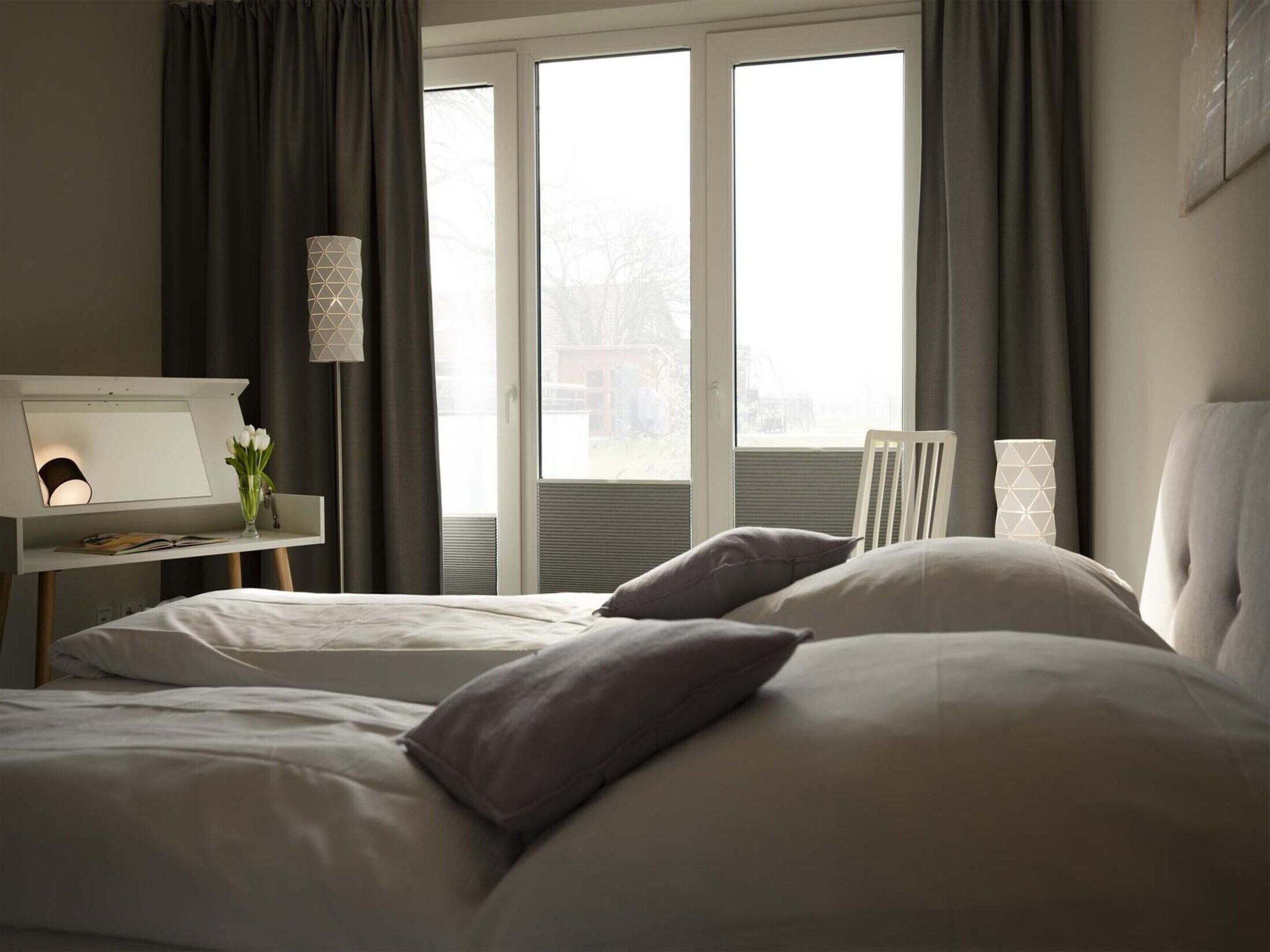 Un dormitorio con una cama, una mesita de noche con lámpara y una ventana con cortinas.