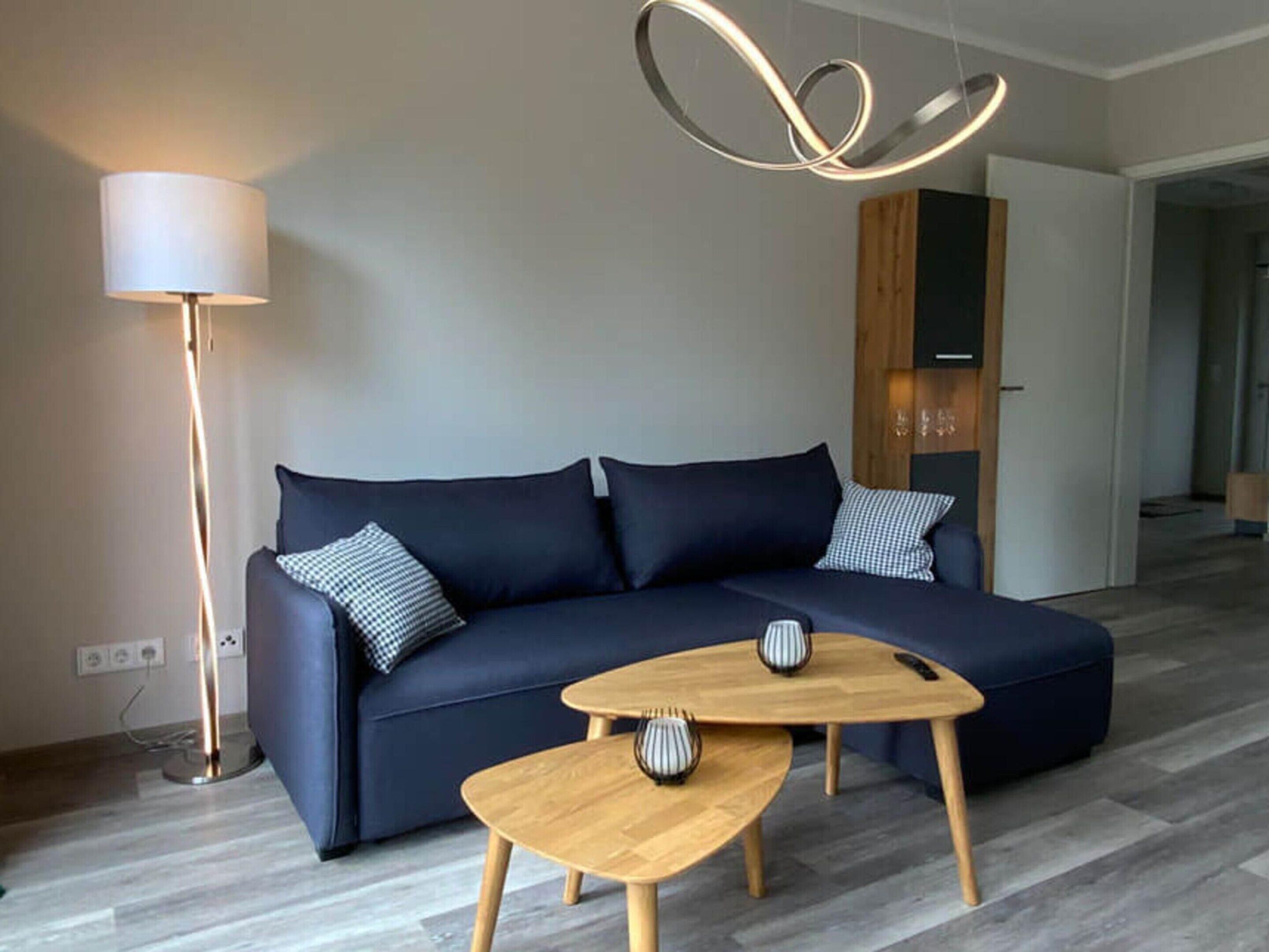 A modern living room with a dark blue sofa, two wooden coffee tables, a floor lamp, and a unique ceiling light fixture.