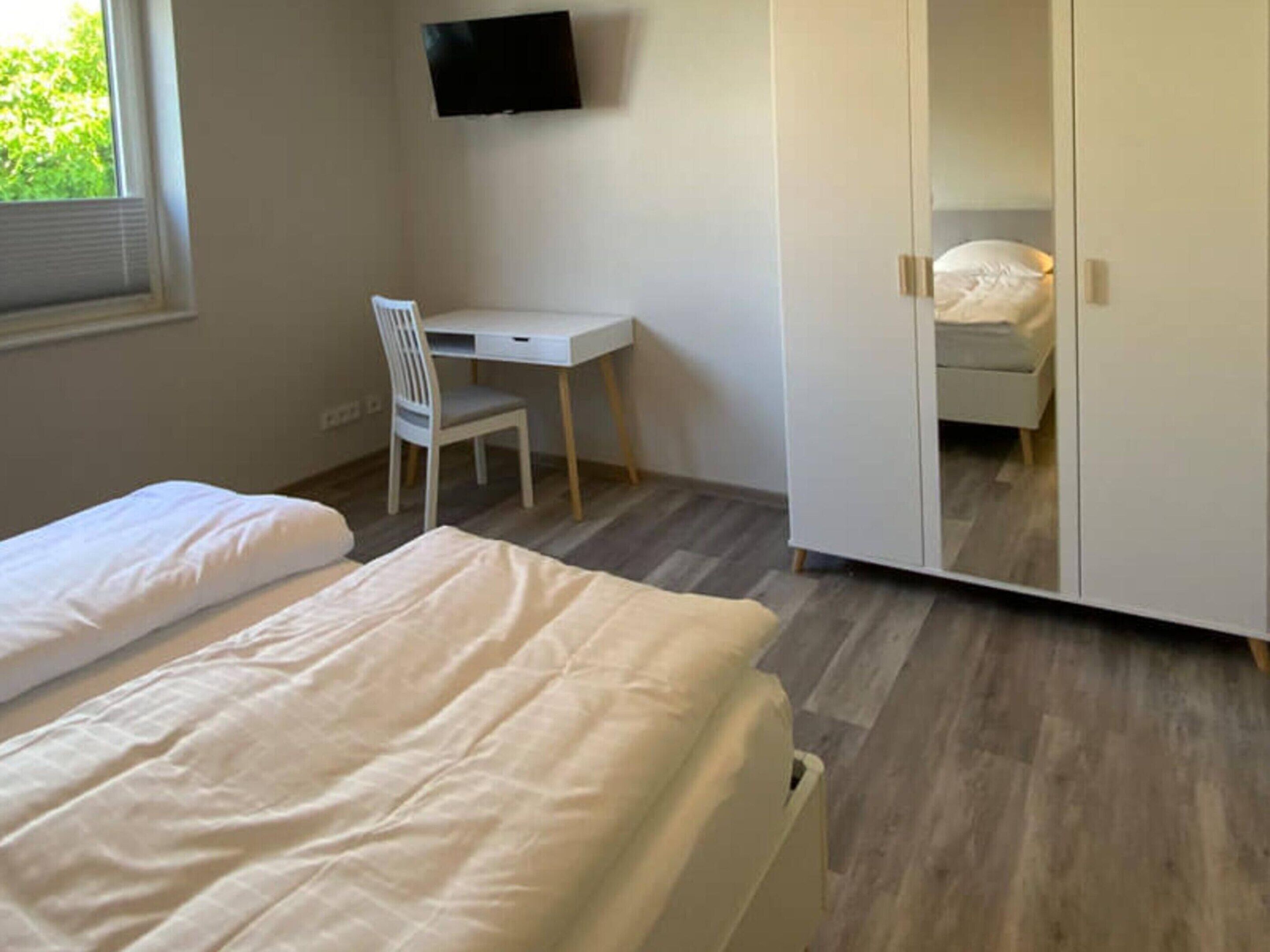 Une chambre avec deux lits, un bureau, une chaise, une armoire et un téléviseur fixé au mur.