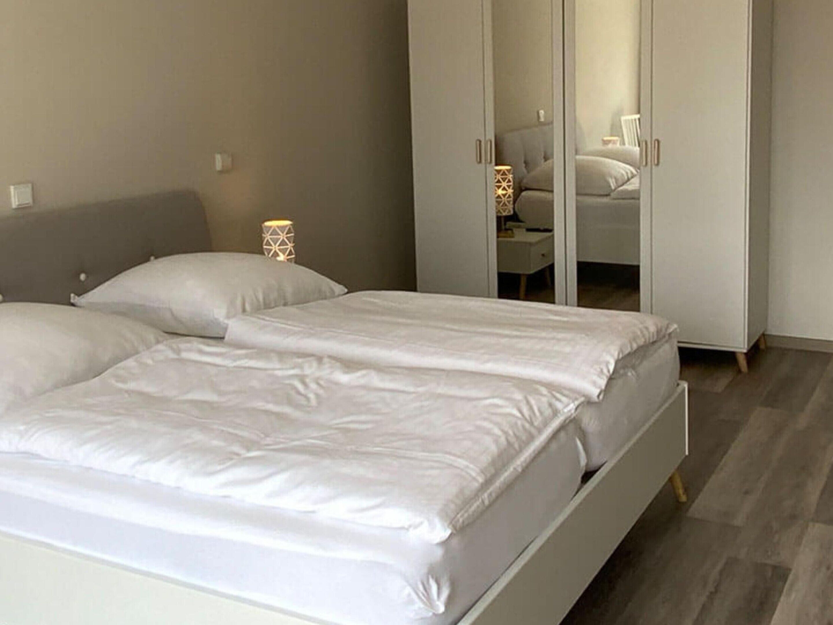 A bedroom with a bed, a wardrobe, and a nightstand with a lamp.