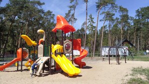 Une aire de jeux avec des toboggans et des structures d’escalade, entourée d’arbres.