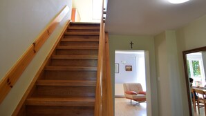 A wooden staircase with a handrail, leading to a room with a cross on the wall, a chair, and a table. - Large House by the Lake, Kashubia (Parchowo)
