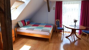 A bedroom with a sloped ceiling, a bed with a colorful quilt, a wooden chair, a small round table with a vase, and a window with red curtains. - Large House by the Lake, Kashubia (Parchowo)