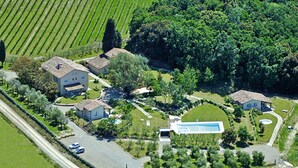 Vue aérienne d’une propriété comprenant plusieurs bâtiments, une piscine et de vastes espaces verts environnants.