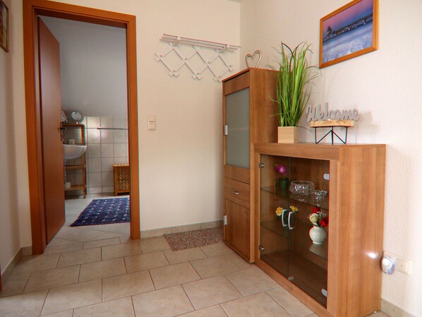 A hallway with a wooden cabinet, a blue rug, and a welcome sign. - Appartementhaus Nicole, Zinnowitz (Zinnowitz)
