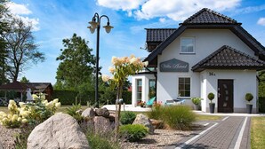 A villa named Villa Astrid with a paved pathway leading to the entrance, surrounded by large rocks and plants.