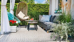 A cozy outdoor seating area with a wicker chair, a cushioned bench, and a sofa.