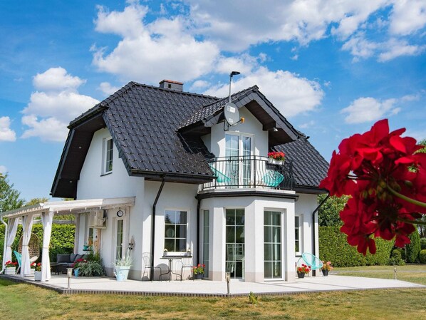 Une maison moderne à deux étages, dotée d’un grand balcon, d’une terrasse couverte et d’un jardin bien entretenu.