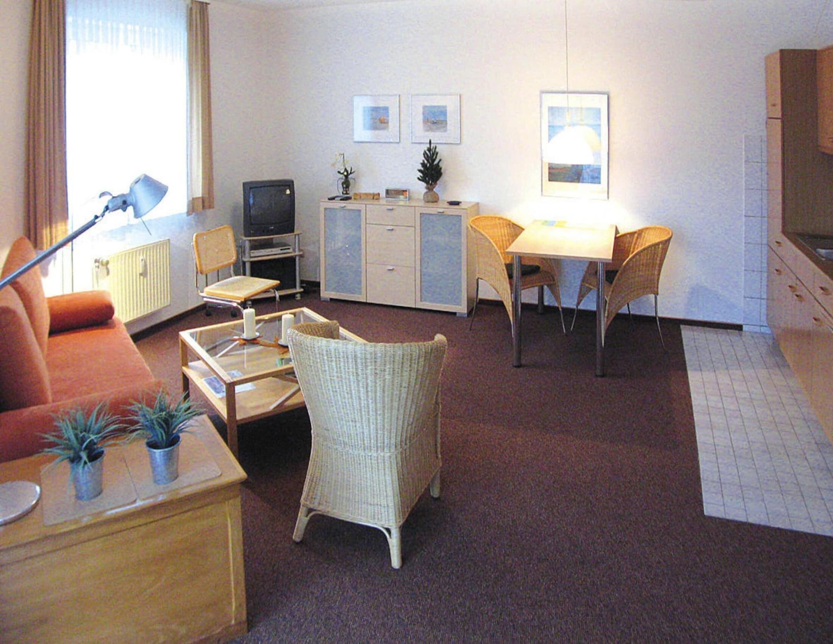 A compact living space with a sofa, a dining table with chairs, a television, a cabinet, and a small kitchenette area.