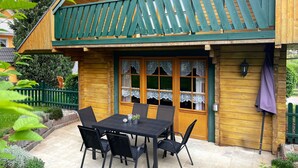 A wooden house with a balcony, a dining table with chairs, and a window with lace curtains. - Blockhouse in the Fuchsbau, Bad Sachsa (Bad Sachsa)