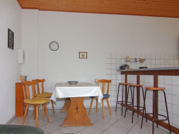 A dining area with a wooden table and chairs, a kitchen counter with stools, and a clock on the wall. - Ferienwohnung im Gutshaus Schulenbrook (Metelsdorf)