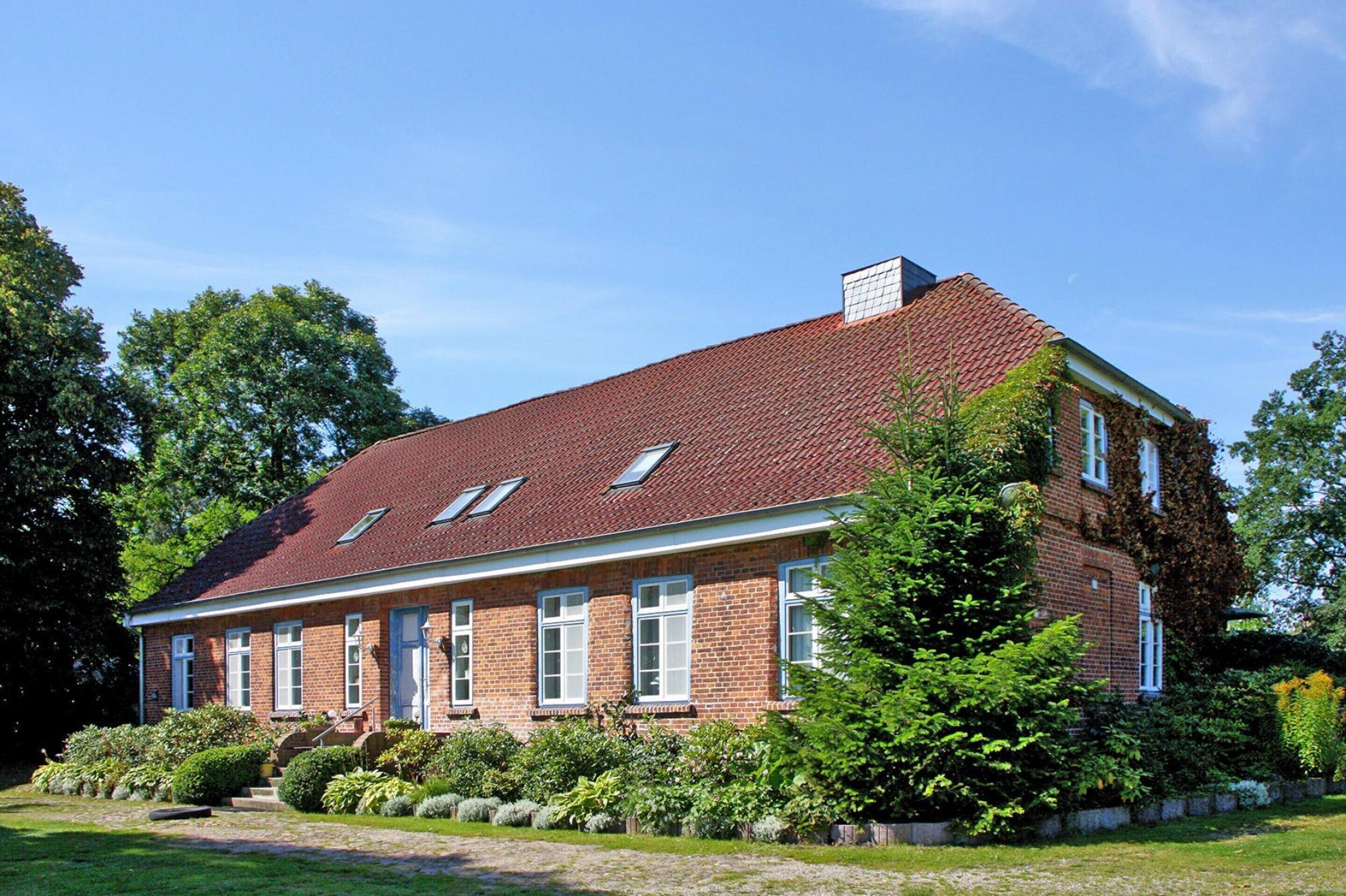 A two-story brick house with a red-tiled roof, multiple windows, and a well-maintained garden.