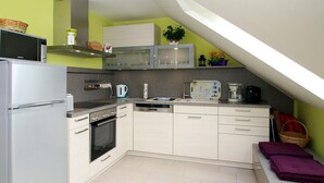A compact kitchen with a refrigerator, stove, microwave, and dishwasher. There is a small seating area with a bench and a basket. - Appartementhaus am Kiessee, Westerholt (Nenndorf)