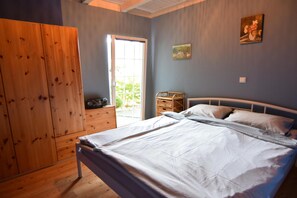 A bedroom with a bed, a wooden wardrobe, a small table with a radio, and a window with a view of greenery. - House With Private Beach by the Lake, Whirlpool (Gniewino)