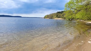 Un lac aux eaux limpides, avec une plage de sable et des arbres qui bordent la rive droite.