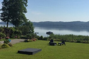 A grassy outdoor area with a view of a lake and hills in the distance. There are two lounge chairs and a small table. - House With Private Beach by the Lake, Whirlpool (Gniewino)