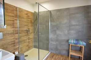 A modern bathroom with a glass-enclosed shower, wooden wall paneling, and a small wooden stool with a colorful cushion. - House With Private Beach by the Lake, Whirlpool (Gniewino)