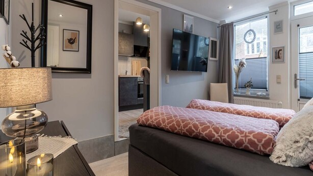 A modern bedroom with a large bed, a TV, and a view of the city. - Ferienwohnung in Tonning (Toenning)