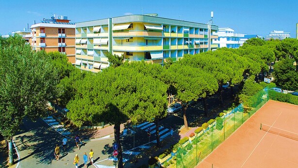 A multi-story building with balconies, surrounded by trees and a tennis court. - Condominio Vera Cruz in Bibione-ex TUI (San Michele al Tagliamento)