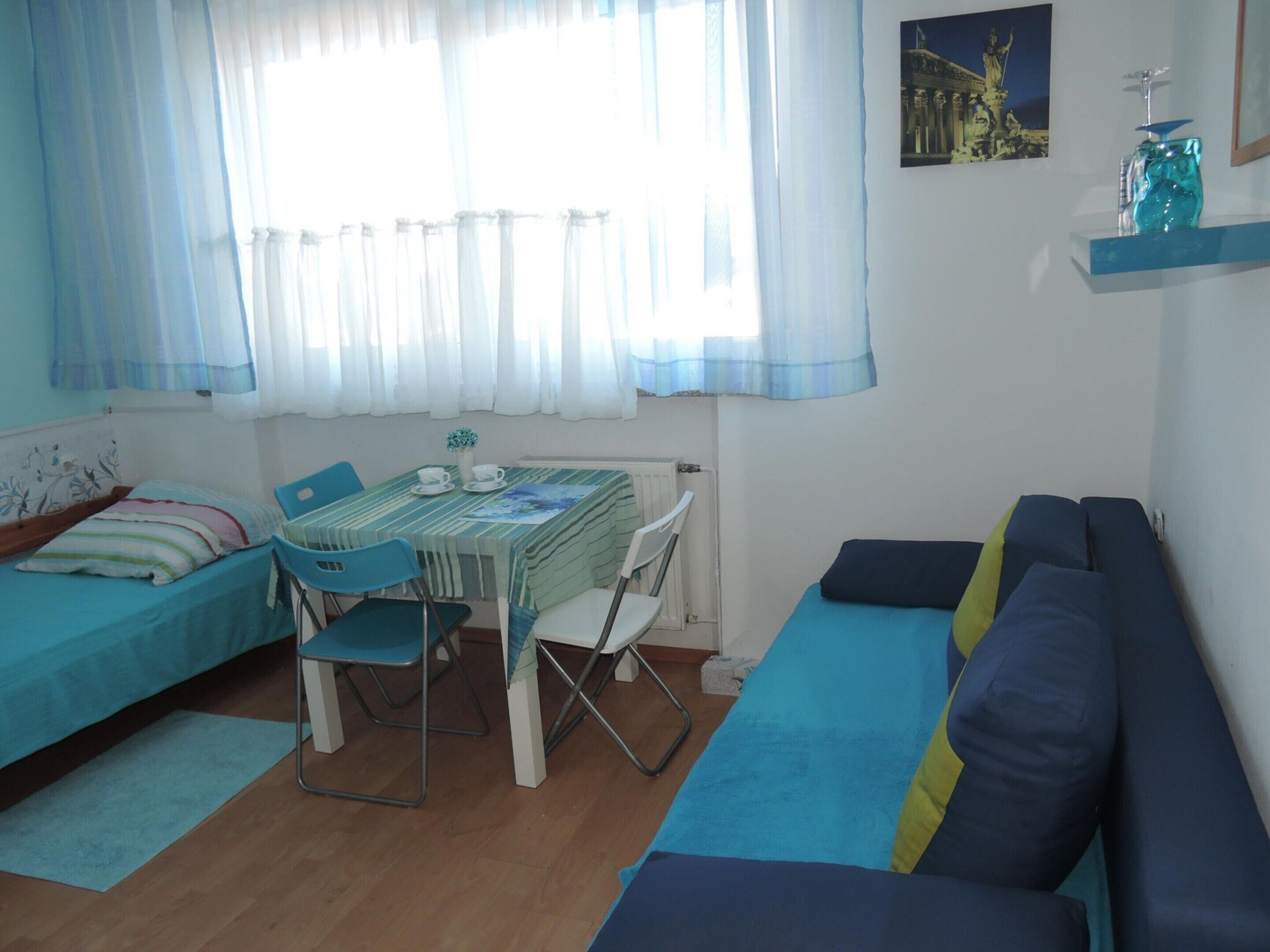 A room with a bed, a sofa, a dining table with chairs, and a window with curtains.