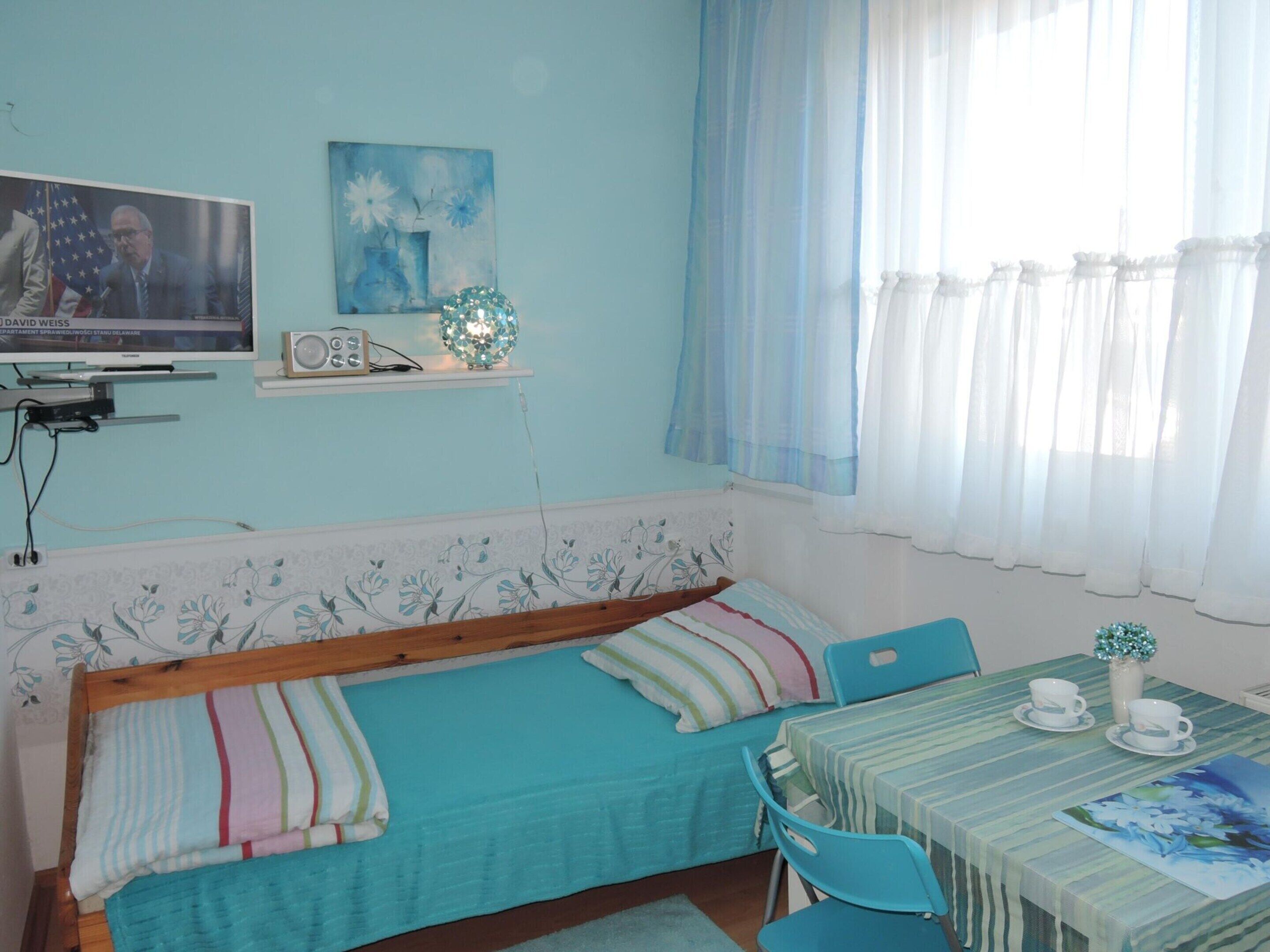 A room with a bed, a TV, a table with cups, and a window with curtains.