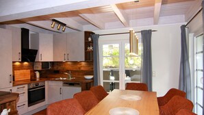 A modern kitchen with wooden cabinets, a built-in oven, and a dining area with a wooden table and cushioned chairs. - Doppelhaushalfte Dunenhaus II, Trassenheide (Trassenheide)