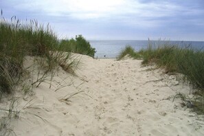 Un sentier de sable qui longe la plage et mène à la mer, bordé d’herbe.