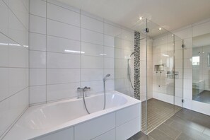 Un baño moderno con una bañera grande, zona de ducha con mampara de cristal y paredes con azulejos blancos.