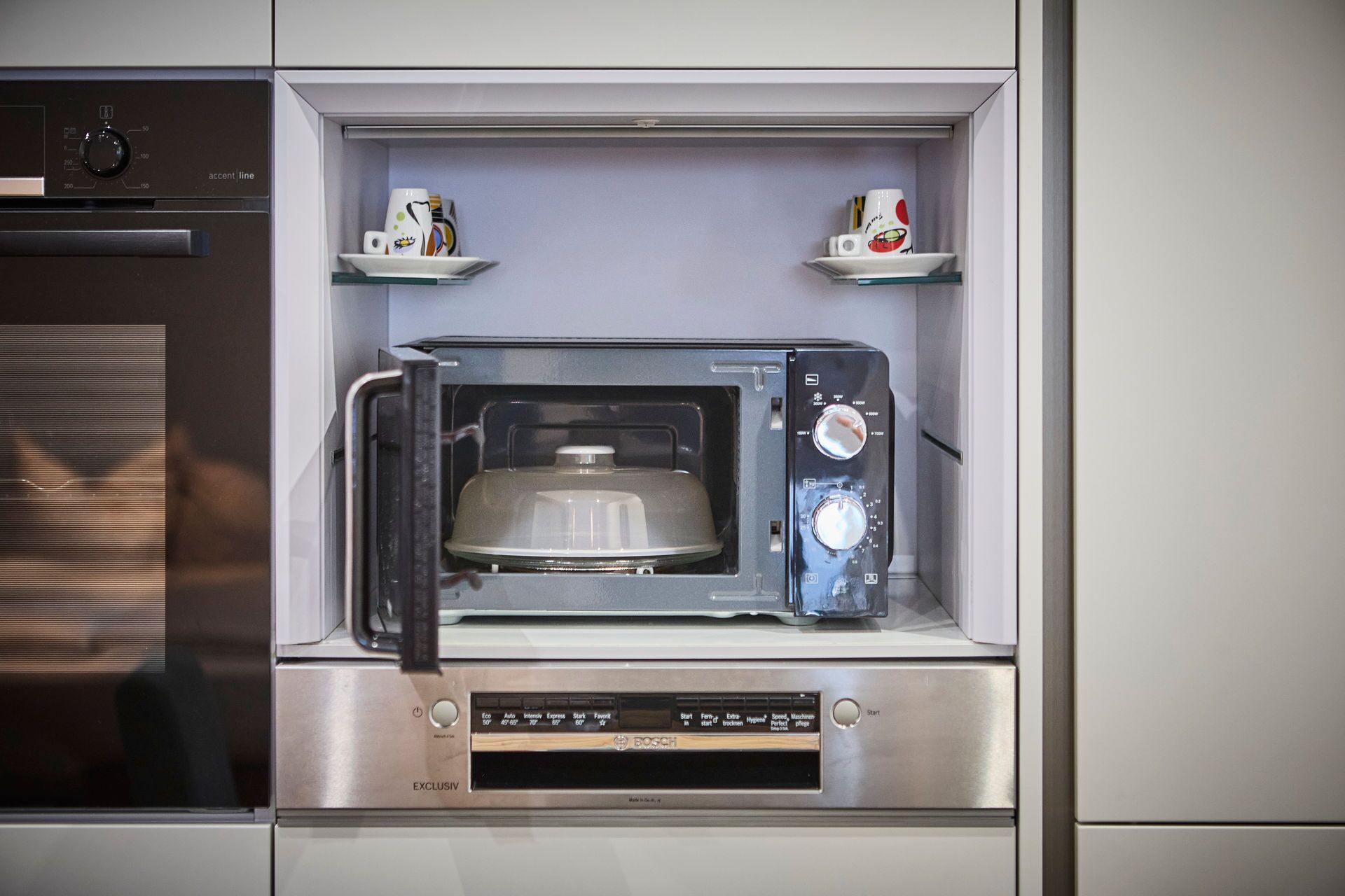 A compact microwave oven with a digital display and control panel, housed in a stainless steel cabinet with a glass door.