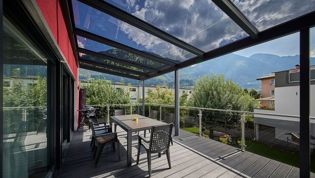 Ein überdachter Außenbereich mit Tisch und Stühlen mit Blick auf eine Berglandschaft.